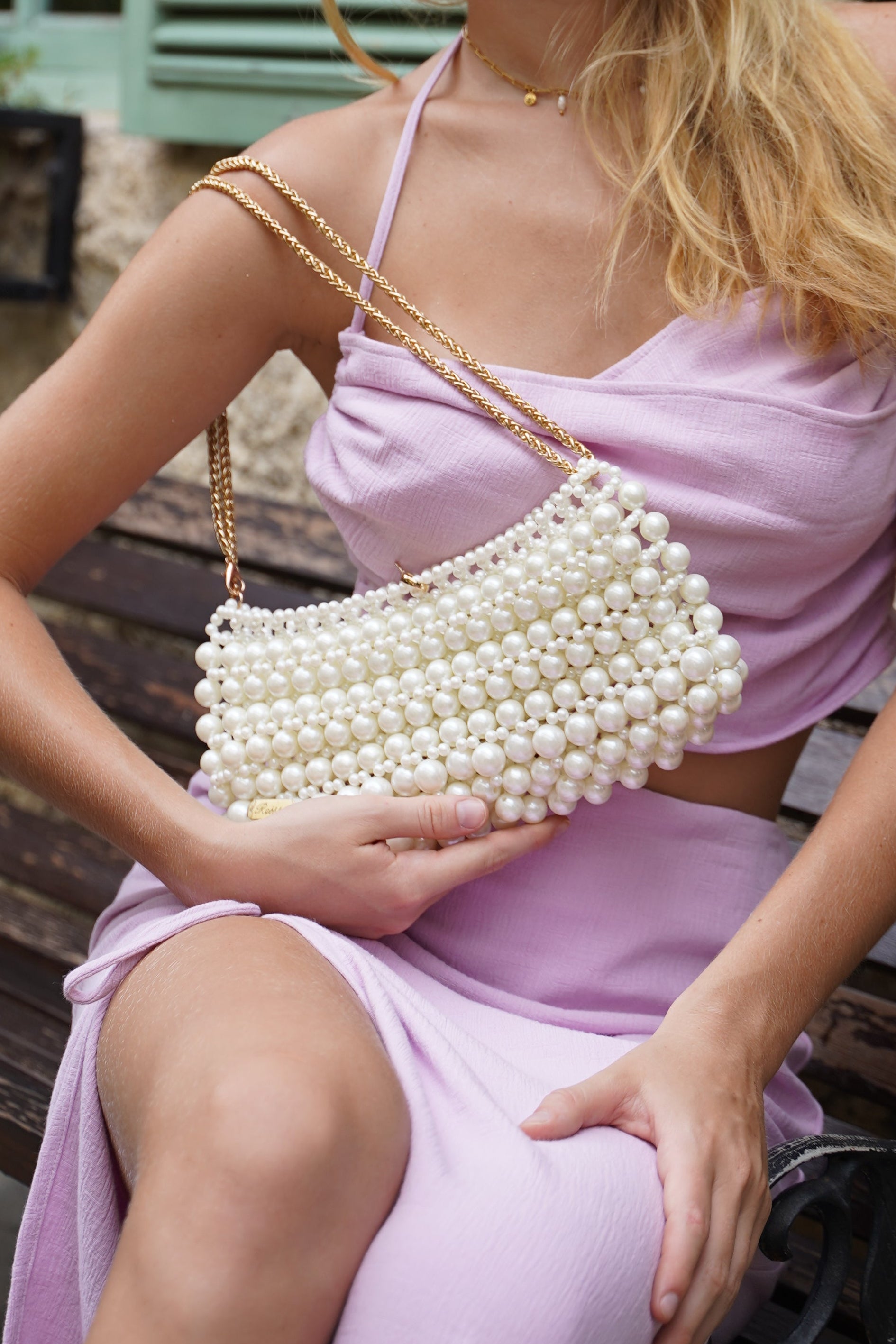 Woman in a pink dress holding a pearl clutch against a rustic background